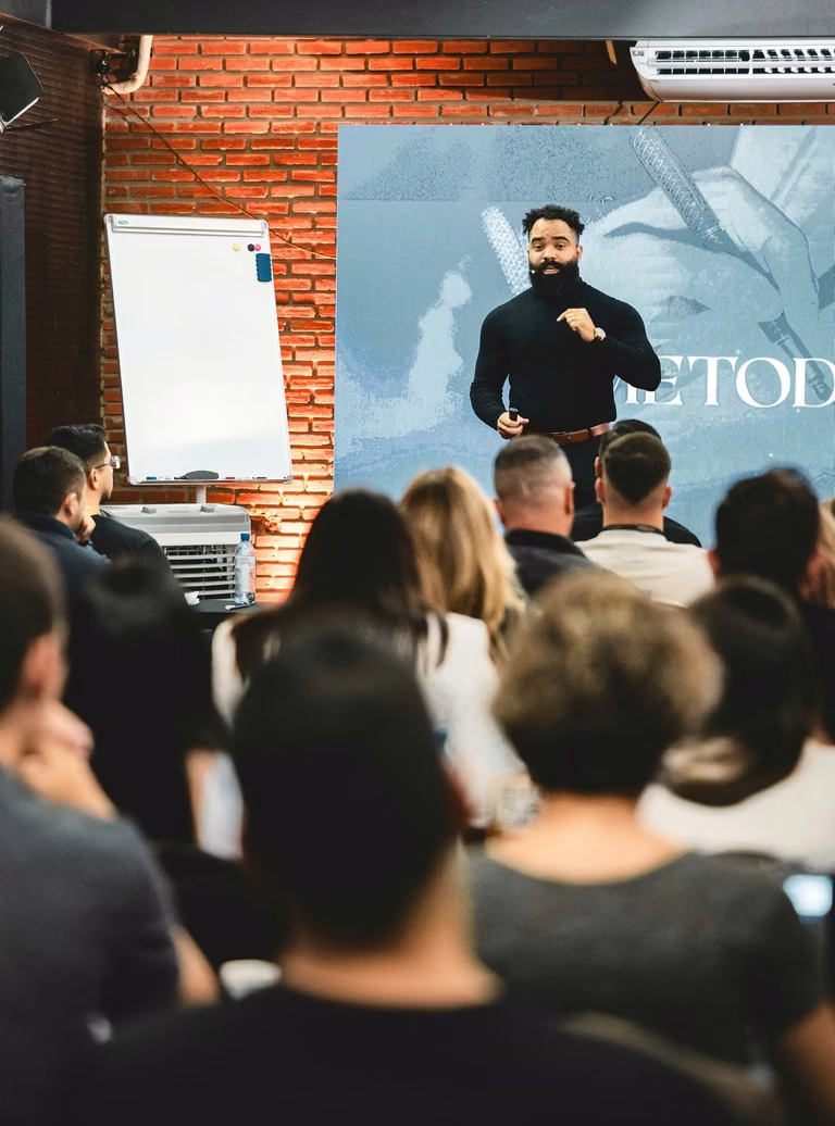 Palestrante conduz a masterclass diante do telão, visto por sobre a plateia de líderes